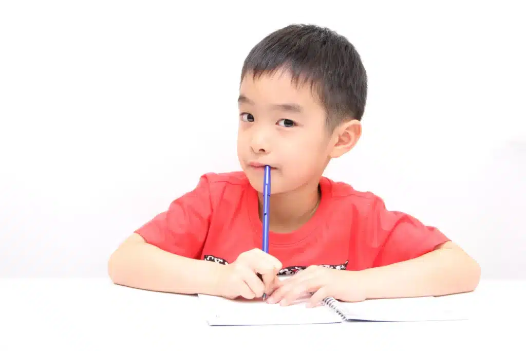 A young boy writing with a blue pen on a white background.