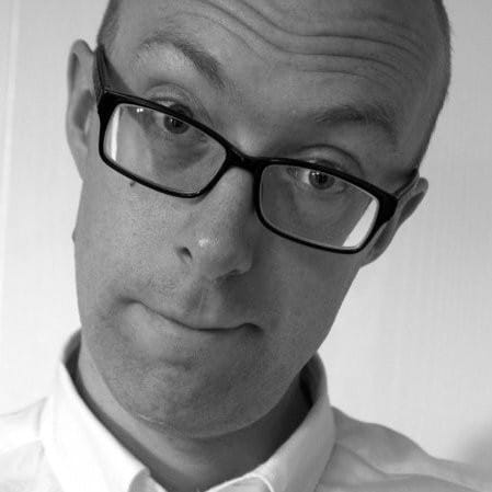 A man with glasses, wearing a white shirt, looks into the camera with a slightly raised eyebrow, as if questioning the environmental impact of our actions. The image is in black and white.