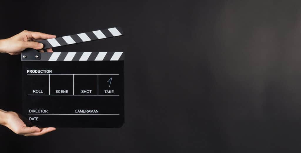 A person holding a movie clapper board against a black background.