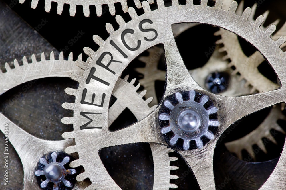 A close up of gears with the word metrics written on them, emphasizing the importance of tracking performance and meeting quotas efficiently.