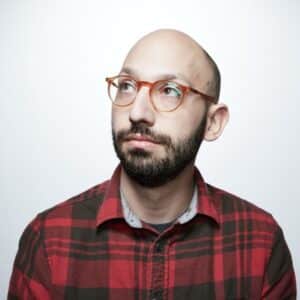A bald man, part of the Ops Teams, wearing glasses and a plaid shirt, hosts a podcast discussing pets.