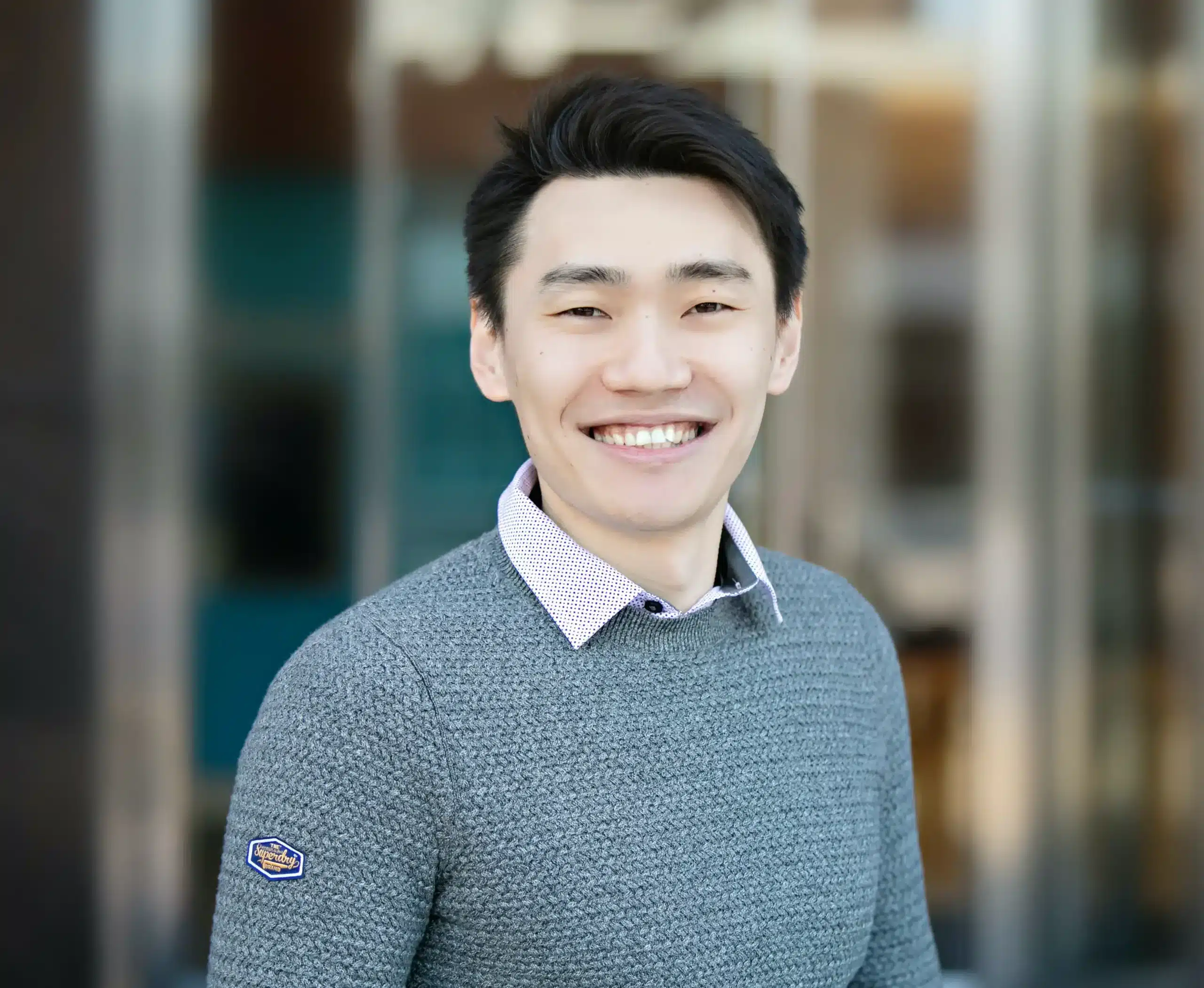 An asian man smiling in front of a building, attending a webinar on cloud native observability to drive business transformation.