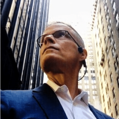 A man in glasses standing in a city, driving business transformation.