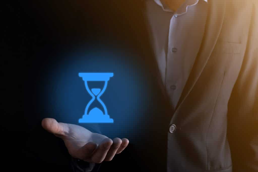 A businessman holding an hourglass in his hand, working to reduce the mean time to remediate.