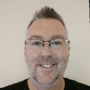 Man with short gray hair, glasses, and light facial hair, smiling against a beige background—ready to discuss Fluent Bit and telemetry data.