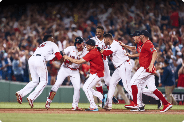 A group of Boston Red Sox baseball players celebrate on the field, smiling and gathering around a teammate, with a cheering crowd in the background, creating a festive scene reminiscent of LOGSapalooza.